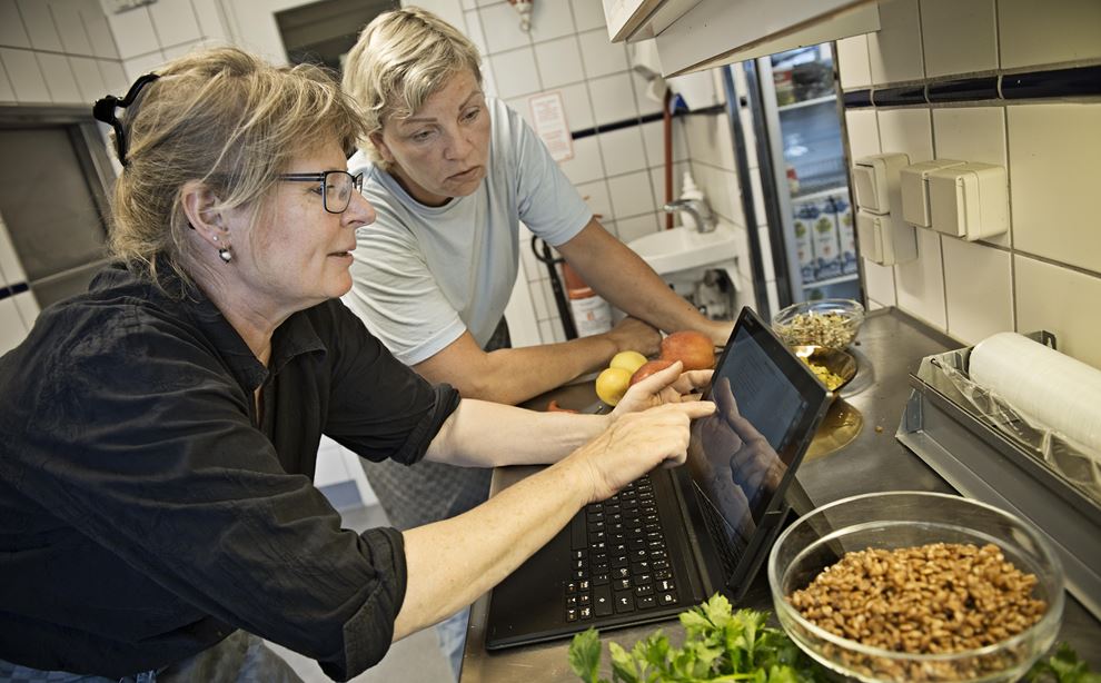 To kvindelige køkkenmedarbejdere ser på en computerskærm, mens de står i køkkenet
